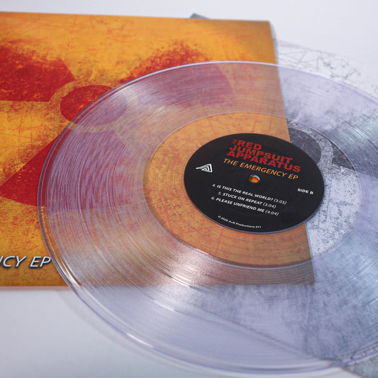 A clear vinyl record with a black center label lies partly on its yellow and orange album cover. Both feature The Emergency EP by The Red Jumpsuit Apparatus.