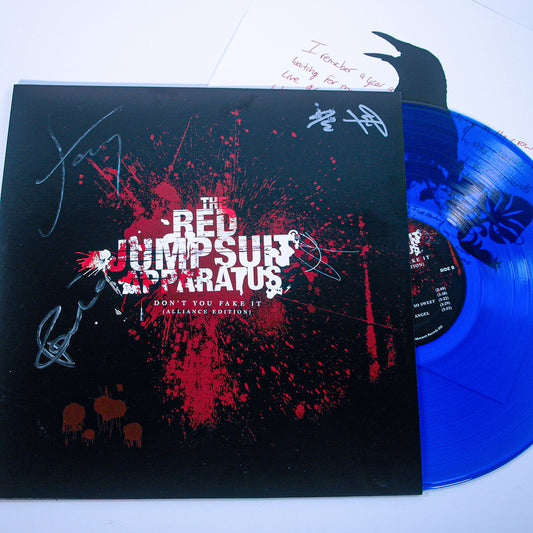A clear blue vinyl record and sleeve for The Red Jumpsuit Apparatus’s Don’t You Fake It, featuring white and red splatter art, band signatures, handwritten lyrics, and a partially visible handwritten note in the background.